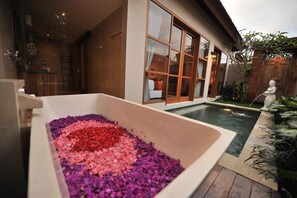 A modern house with a large glass window, a small pool, and a flower bed.