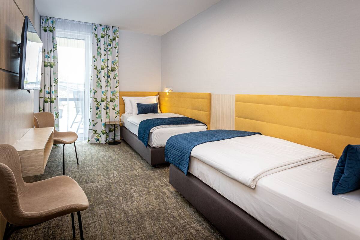 Ein Hotelzimmer mit zwei Betten, einem Schreibtisch, einem Stuhl und einem Fernseher.