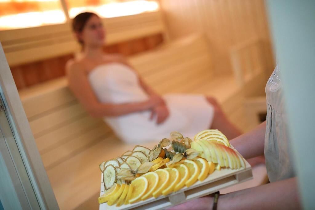 Spa-miljø med en person i håndklæde, en bakke med frugt og en træbænk.