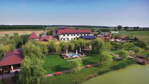 A large building with multiple red-roofed structures, a swimming pool, and a surrounding garden with pathways and seating areas. - Nádas Tó Park Hotel (Vasad)