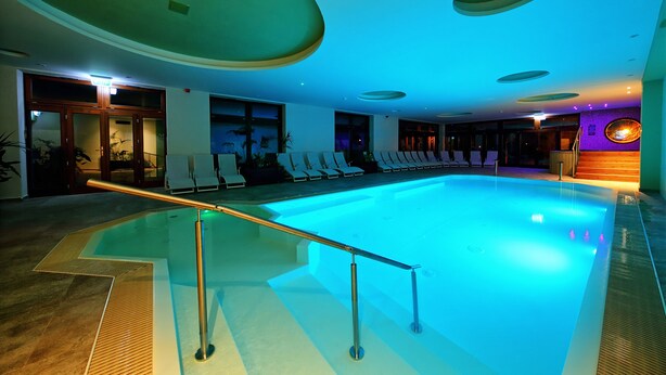 A swimming pool with a glass barrier, lounge chairs, and a reception area with a sign. - Nádas Tó Park Hotel (Vasad)
