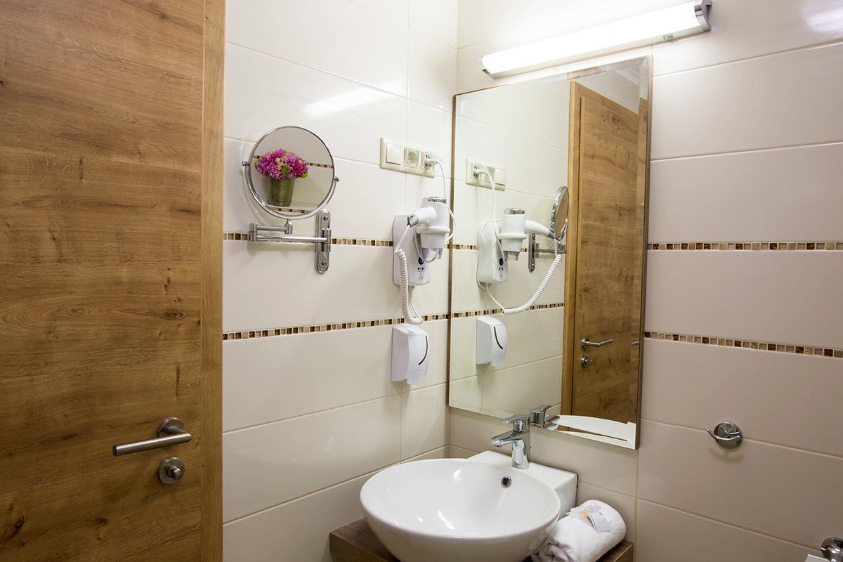 A bathroom with a wooden door, a round mirror, a sink, and two hair dryers mounted on the wall.