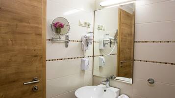 A bathroom with a wooden door, a round mirror, a sink, and two hair dryers mounted on the wall.