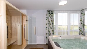 A sauna room with a wooden bench, a glass door, and a view of the outdoors through large windows. - Nádas Tó Park Hotel (Vasad)