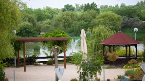 A gazebo, a pergola, and a fountain in a garden setting with a lake in the background. - Nádas Tó Park Hotel (Vasad)