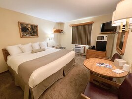 Habitación de hotel con una cama grande, un escritorio con una silla, un televisor, un microondas y una ventana con cortinas.