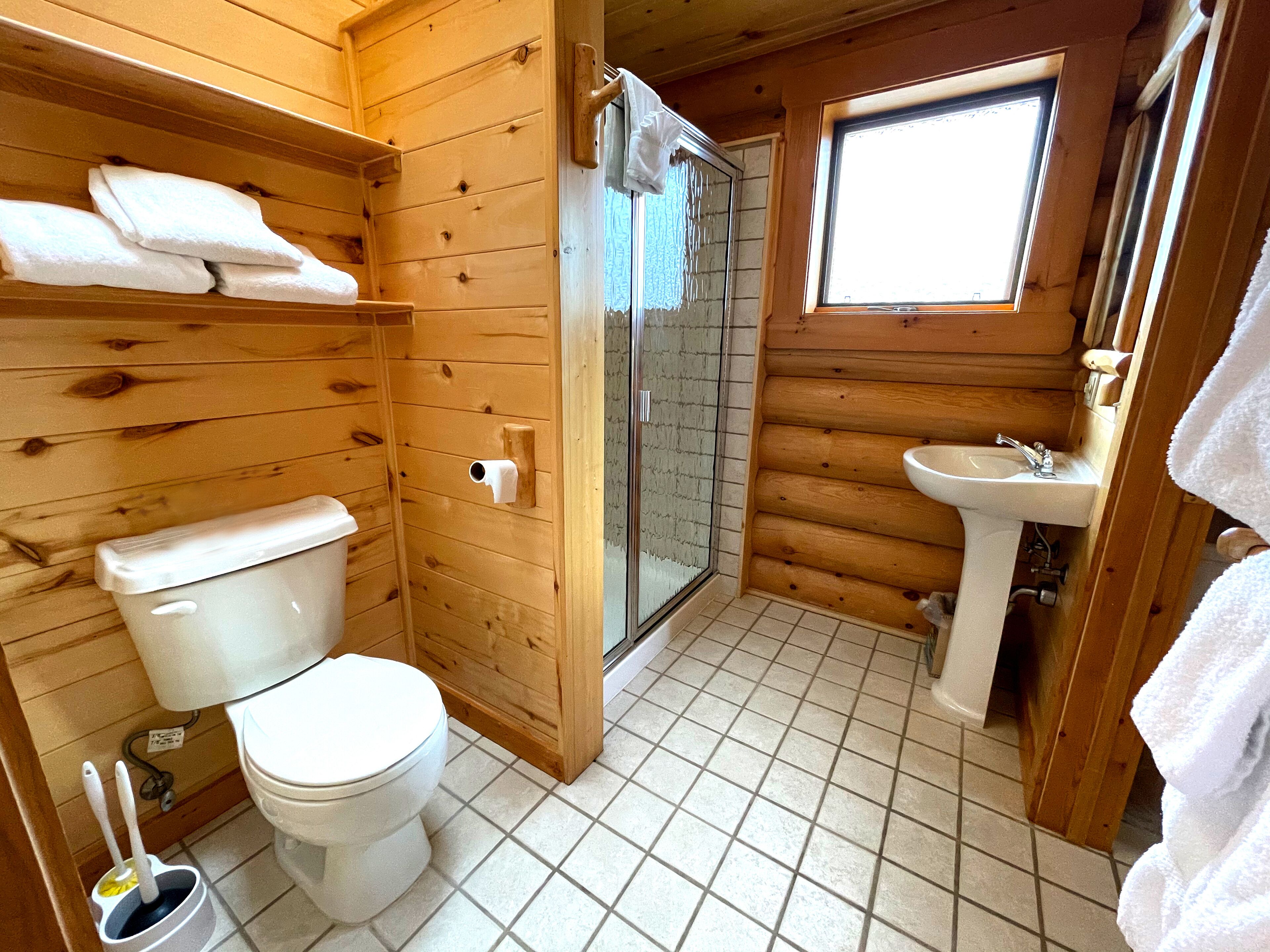 A wooden cabin bathroom with a toilet, shower, and sink.