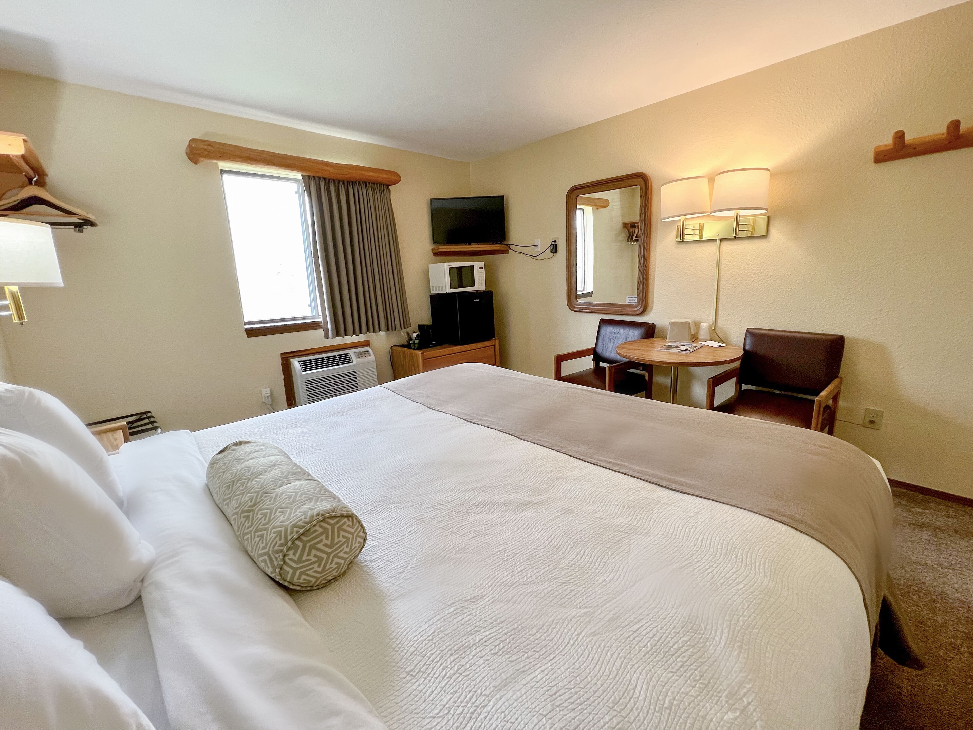 A hotel room with a large bed, a desk, a chair, a television, a mirror, and a lamp.