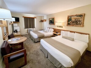 A hotel room with two beds, a desk, a chair, a TV, a painting, and a lamp.