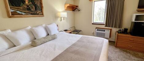 Una habitación de hotel con una cama grande, un cuadro en la pared, una ventana con cortinas, un escritorio con una lámpara y un televisor.