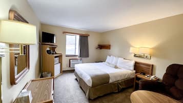 A hotel room with a bed, bedside table, lamp, TV, and a chair.