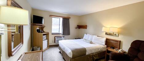 A hotel room with a bed, bedside table, lamp, TV, and a chair.