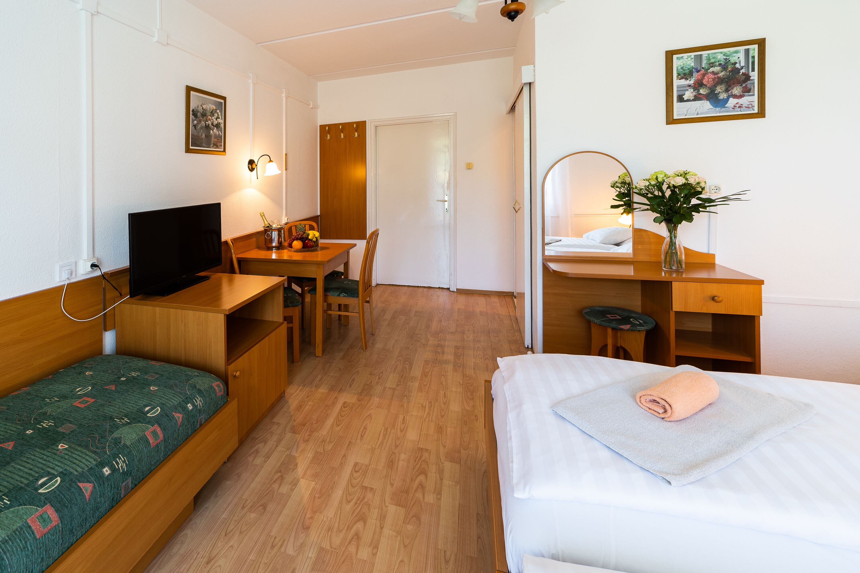 Habitación de hotel con cama, escritorio, silla, televisor y una pequeña mesa con un florero.