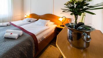 A hotel room with a bed, bedside table, and a nightstand with a lamp. There is a vase with flowers on the nightstand.