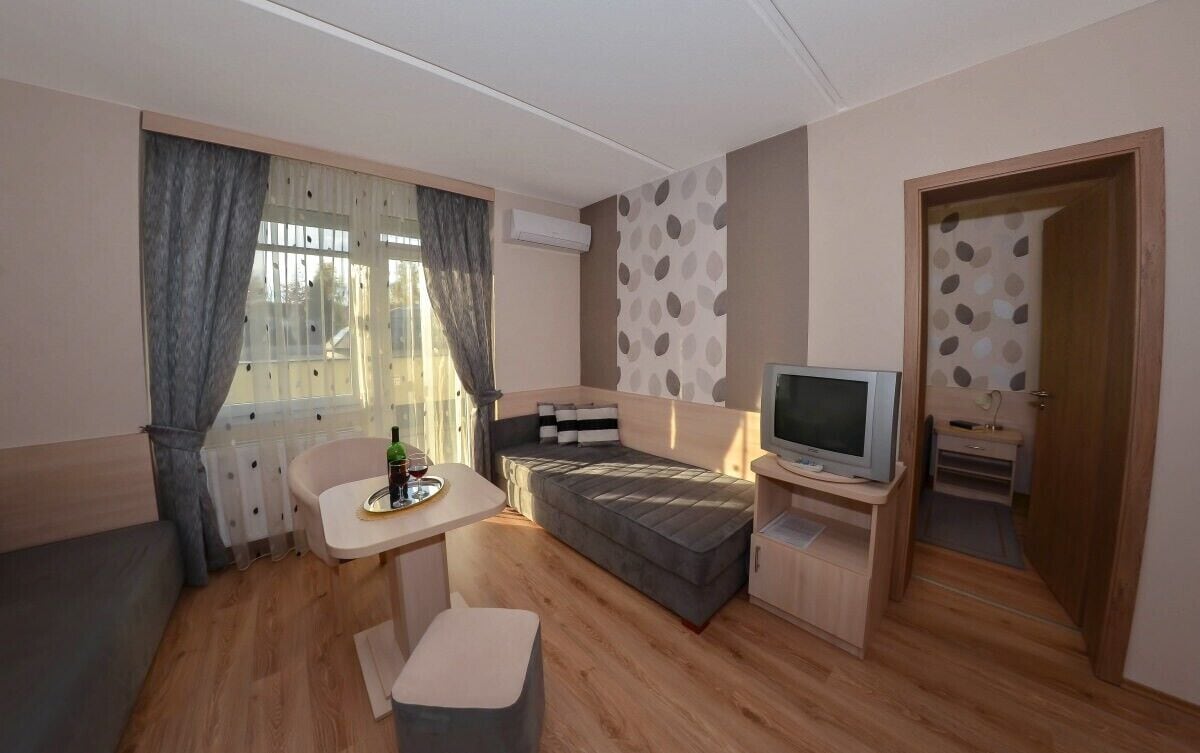 A compact room with a bed, a small table, a TV, and a window with curtains.