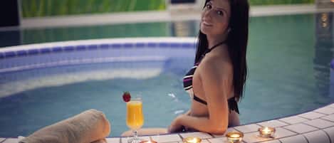 A woman in a swimming pool with a towel, a drink, and candles.