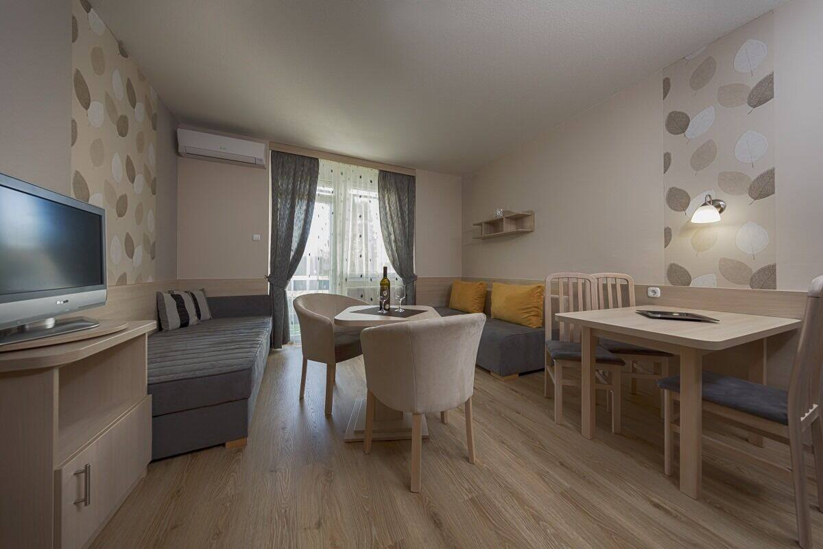 A modern living room with a sofa, dining table, chairs, a TV, and a window with curtains.