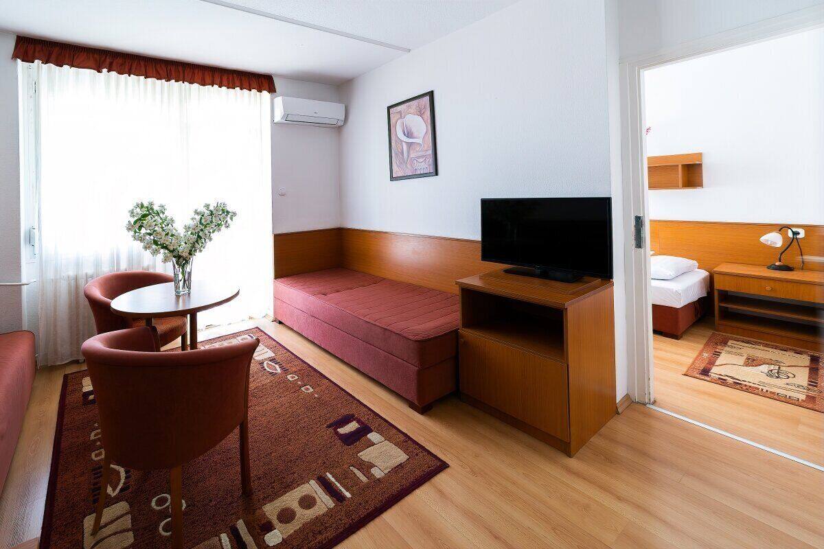 A compact hotel room with a sofa, a small table, a TV, and a wooden desk.