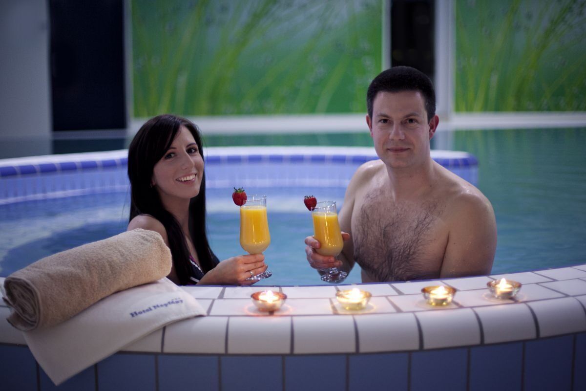 A couple in a hot tub with drinks, candles, and a towel.