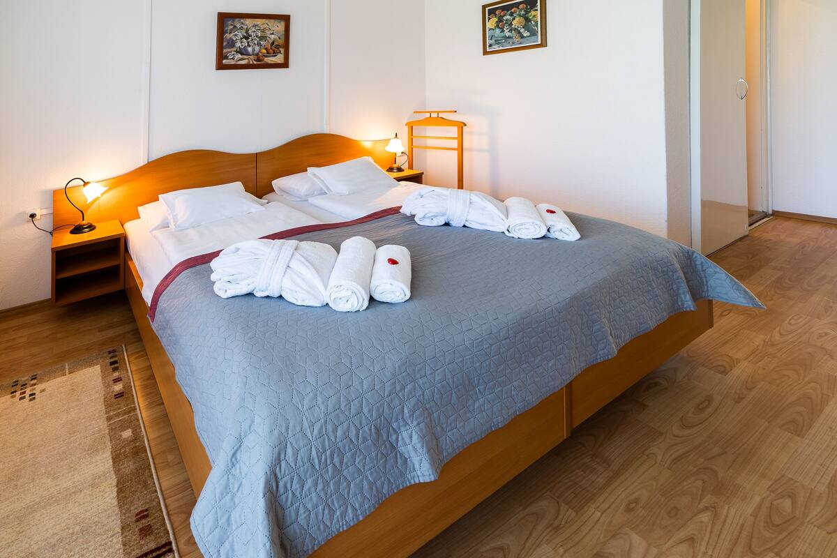 A neatly made bed with white linens and rolled towels, a bedside table with a lamp, and a wooden headboard.