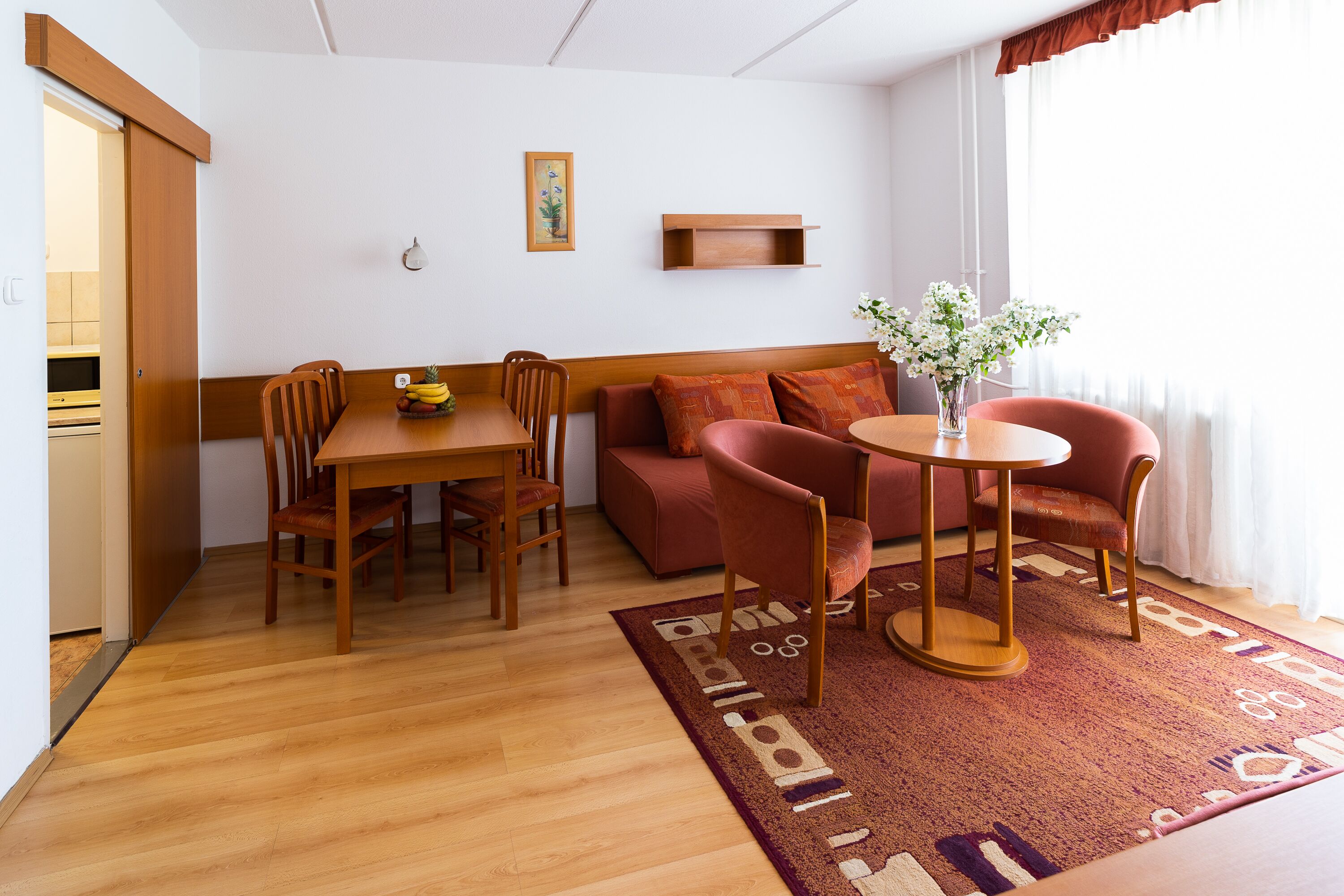 A compact living space with a dining area, a sofa, and a small table with a vase of flowers.
