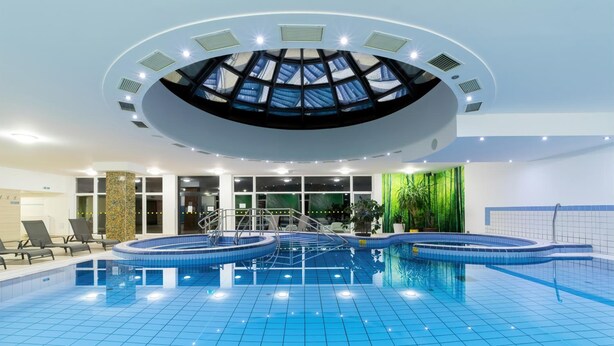 An indoor swimming pool with a skylight ceiling, clear glass walls, and a tiled floor. - Hotel Napfény (Zalakaros)