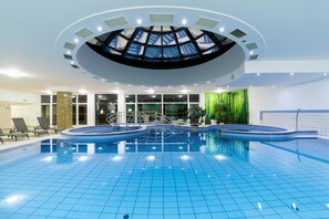 An indoor swimming pool with a skylight ceiling, clear glass walls, and a tiled floor. - Hotel Napfény (Zalakaros)