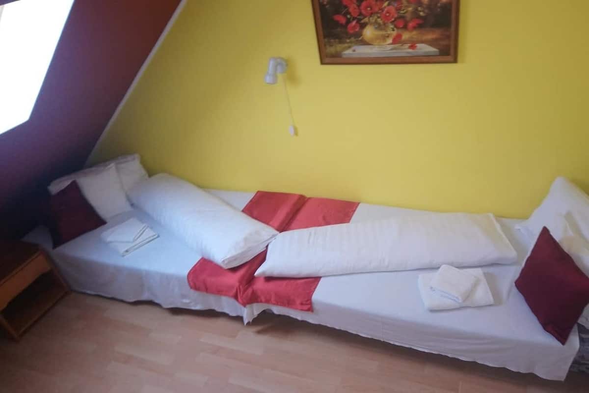 A single bed with white and red bedding, a painting on the wall, and a wooden nightstand.