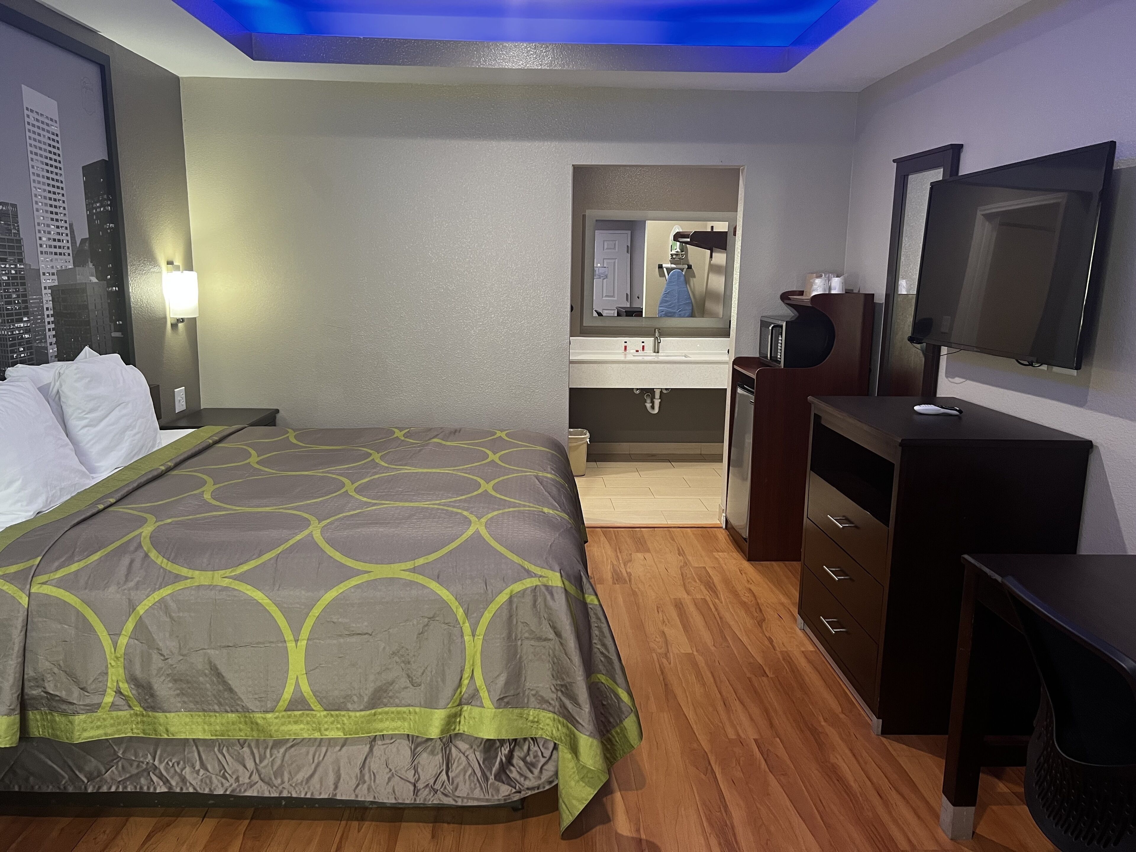 A hotel room with a bed, a desk, a mirror, a TV, and a bathroom visible through an open door.