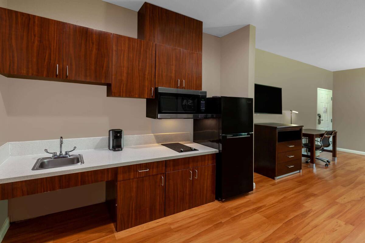 A modern kitchen with wooden cabinets, a stainless steel sink, a microwave, and a refrigerator.