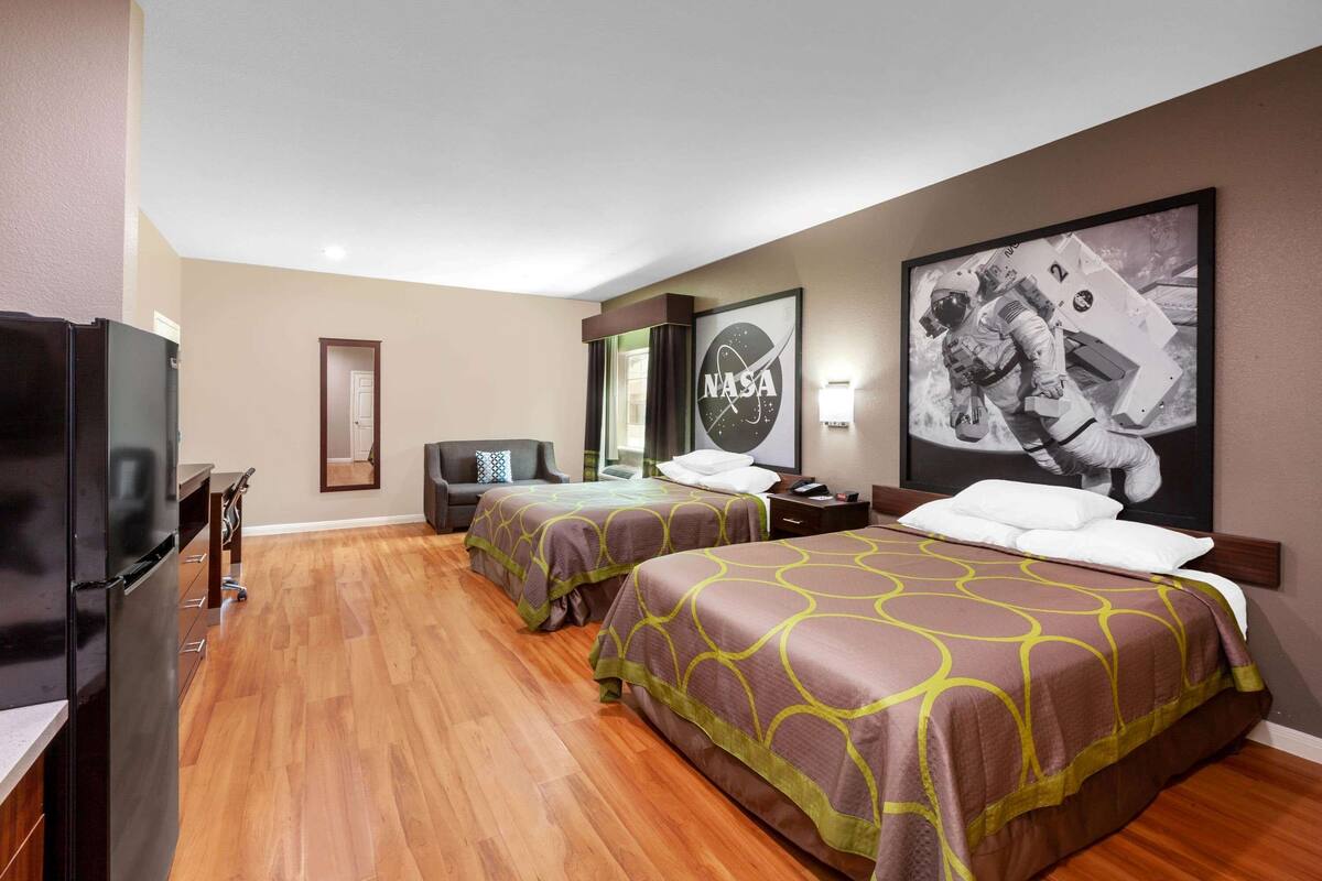 A hotel room with two beds, a TV, a NASA poster, and a wooden floor.