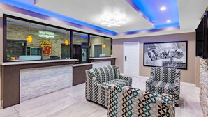 Un vestíbulo de hotel con mostrador de recepción, sillas con estampado, un cuadro enmarcado e iluminación empotrada en el techo.