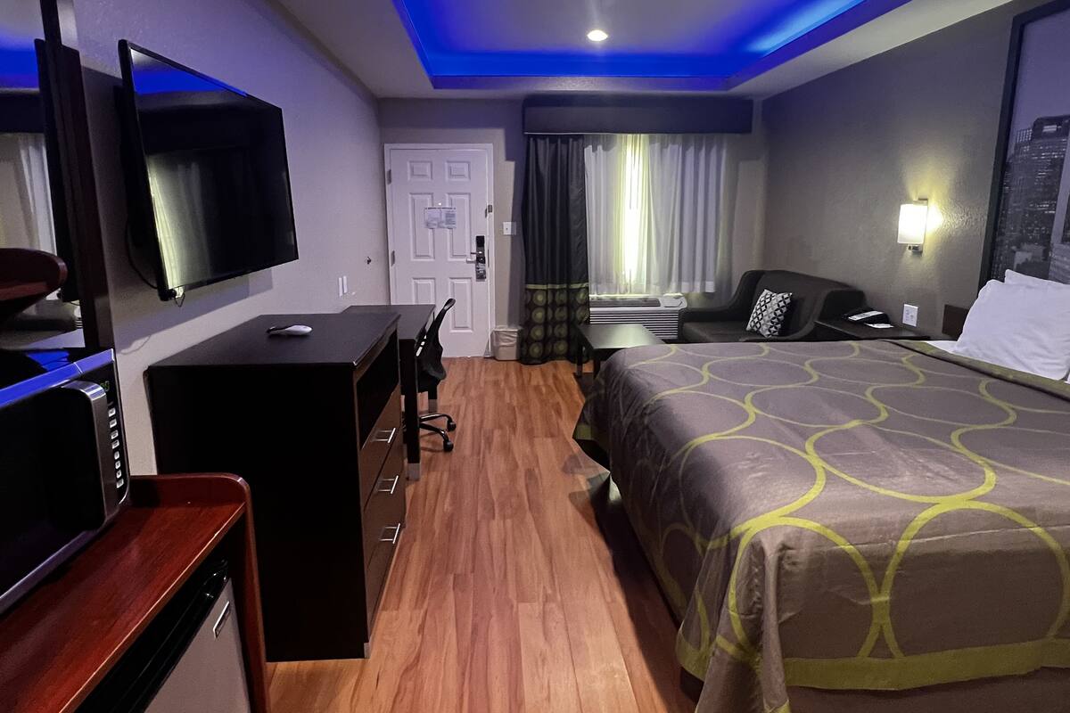 A hotel room with a bed, desk, TV, and a window with curtains.