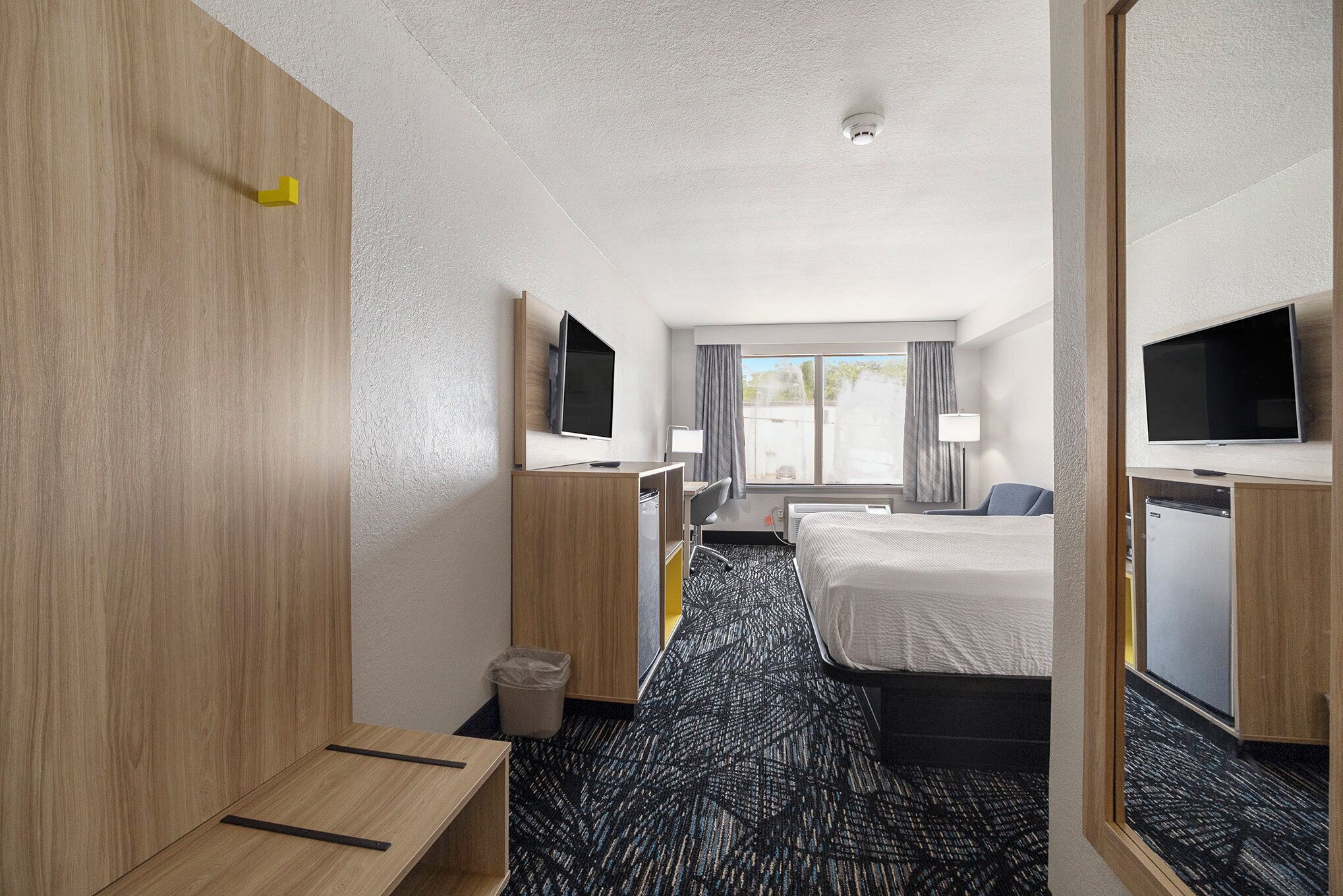 A hotel room with a bed, a desk, a chair, a TV, and a window with curtains.