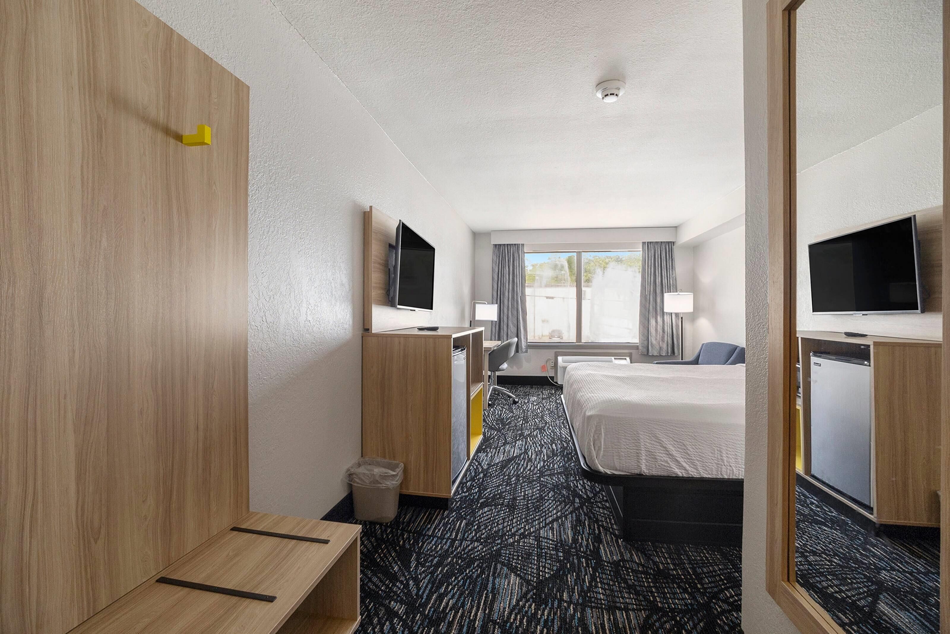 A hotel room with a bed, a desk, a chair, a TV, and a window with curtains.