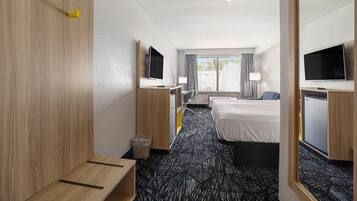 A hotel room with a bed, a desk, a chair, a TV, and a window with curtains.