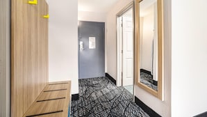 A hallway with a wooden wardrobe, a grey door, a patterned carpet, and a mirror on the wall.
