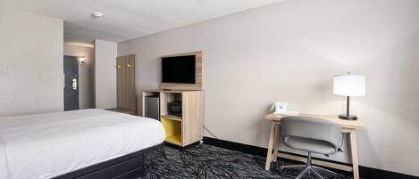 A hotel room with a bed, a desk, a chair, a TV, and a lamp.