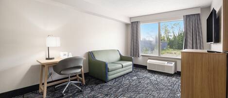 A hotel room with a desk, chair, sofa, and a large window with curtains.