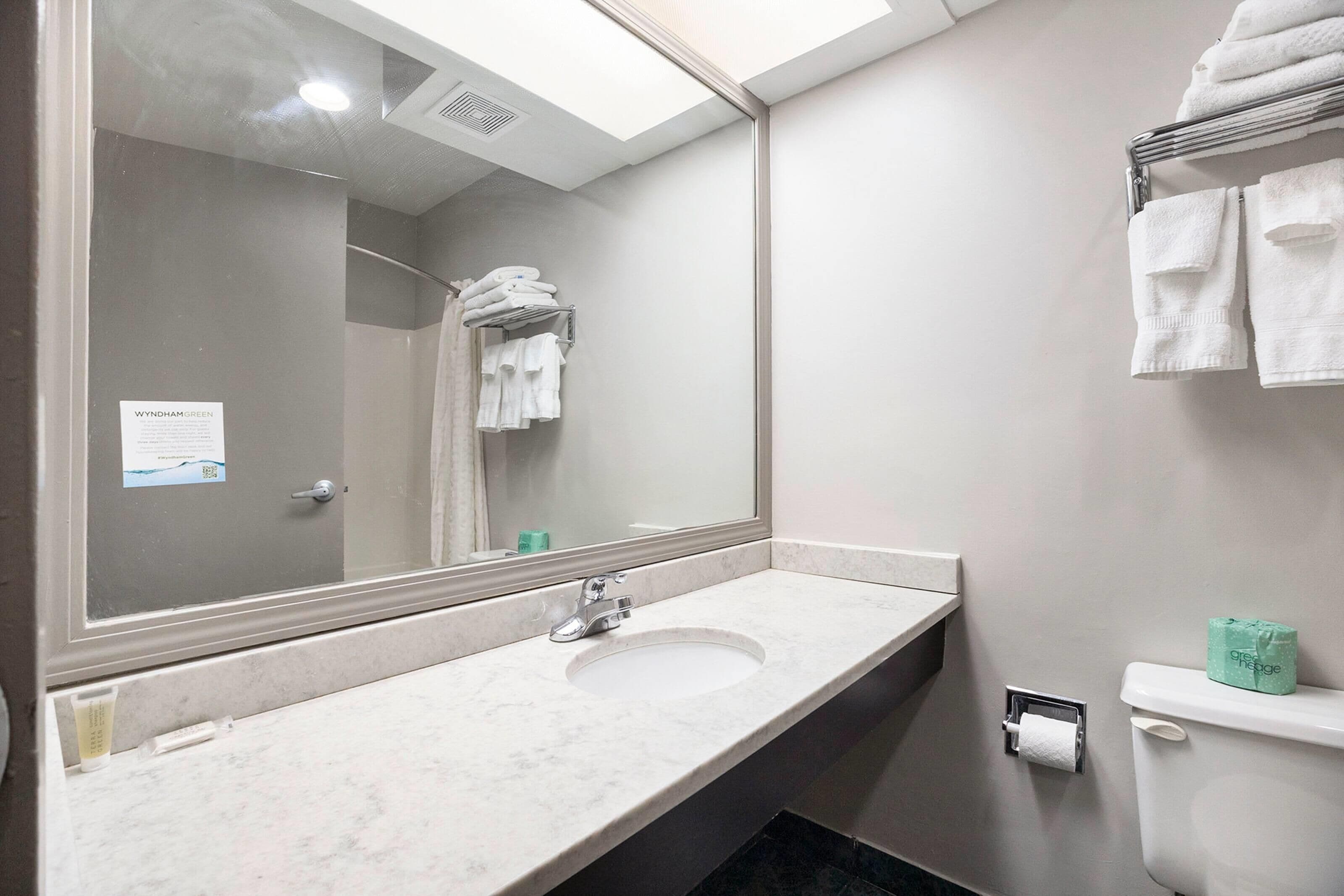 A bathroom with a sink, mirror, towel rack, toilet, and a note on the door.