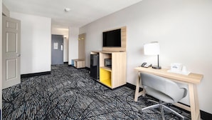 A hotel room with a desk, chair, television, and a small kitchenette.