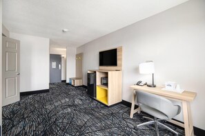 A hotel room with a desk, chair, television, and a small kitchenette. - Days Inn & Suites by Wyndham Norton Shores/Muskegon (Muskegon)