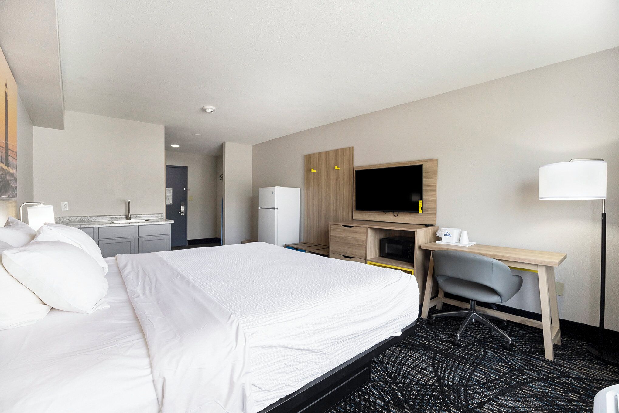 Una habitación de hotel con una cama, un escritorio, una silla, un televisor y una kitchenette.