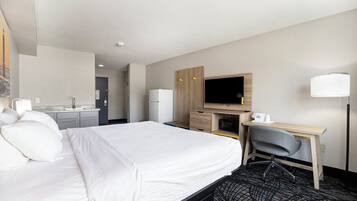 A hotel room with a bed, a desk, a chair, a television, and a kitchenette.