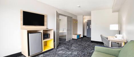 Habitación de hotel con televisión de pantalla plana, refrigerador, sofá, escritorio con lámpara y alfombra estampada.