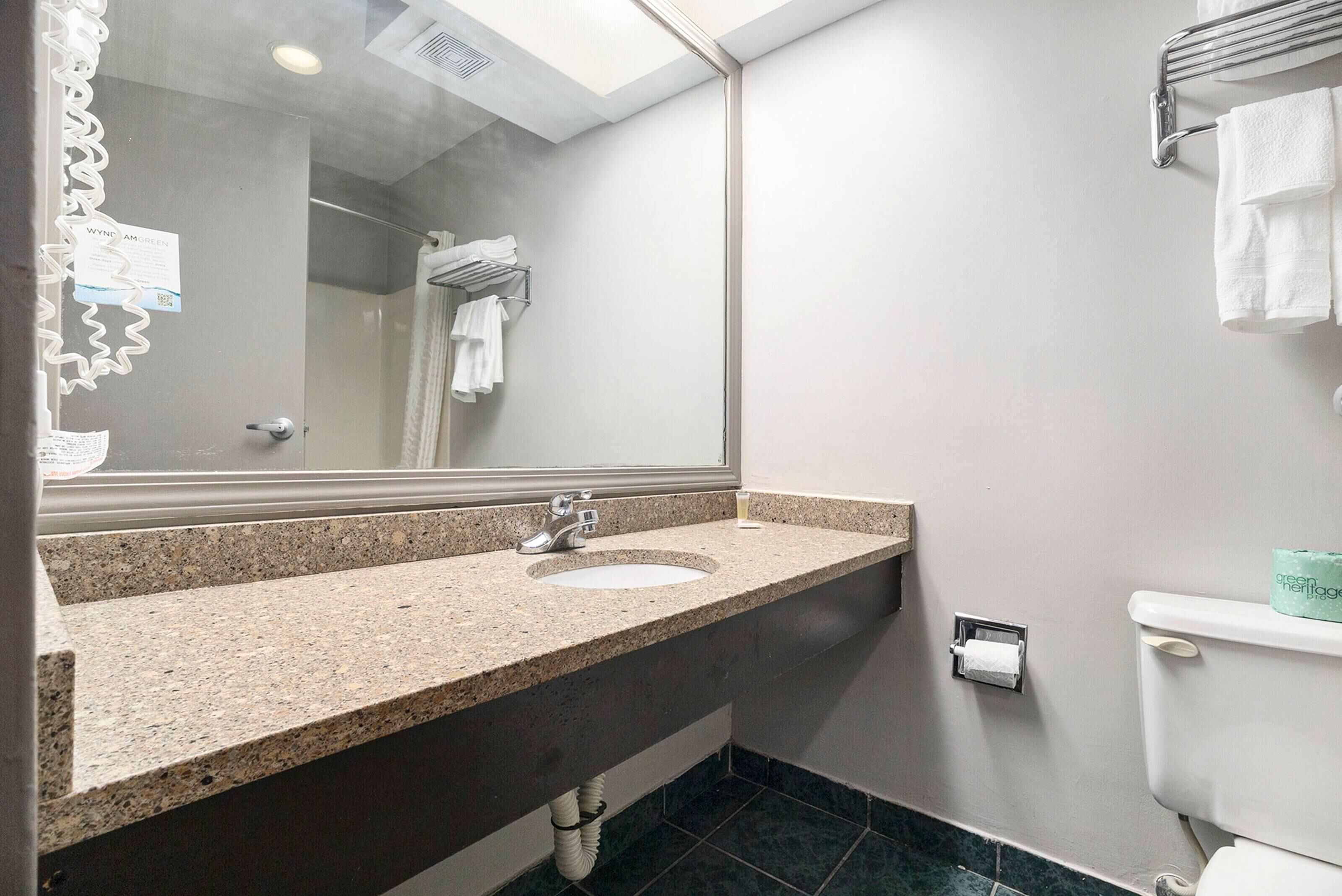A bathroom with a granite countertop sink, a mirror, a towel rack, and a toilet.
