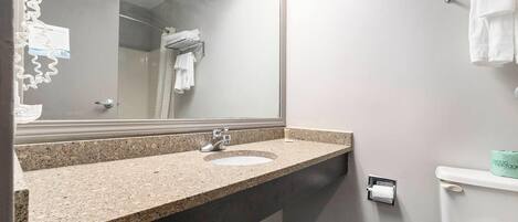 A bathroom with a granite countertop sink, a mirror, a towel rack, and a toilet.