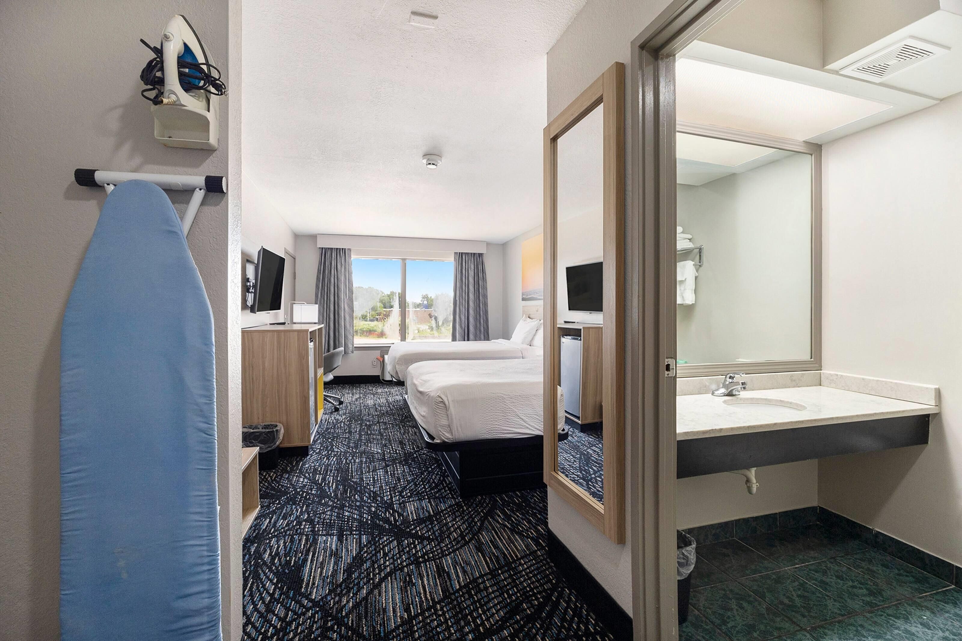 A hotel room with a bed, a desk, a chair, a TV, a bathroom with a sink and mirror, and a window with curtains.