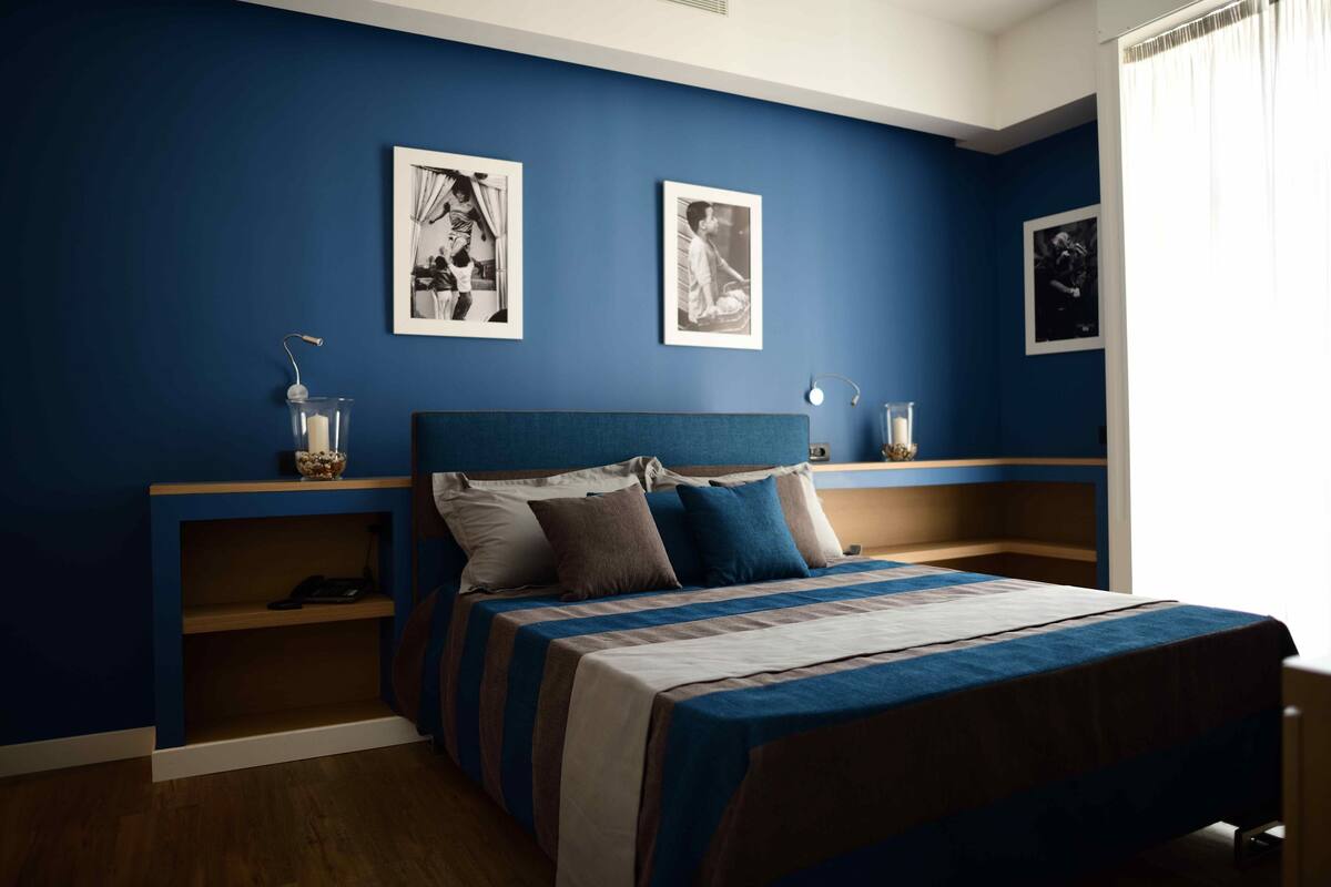 Quarto com uma cama, paredes azuis e três quadros na parede.