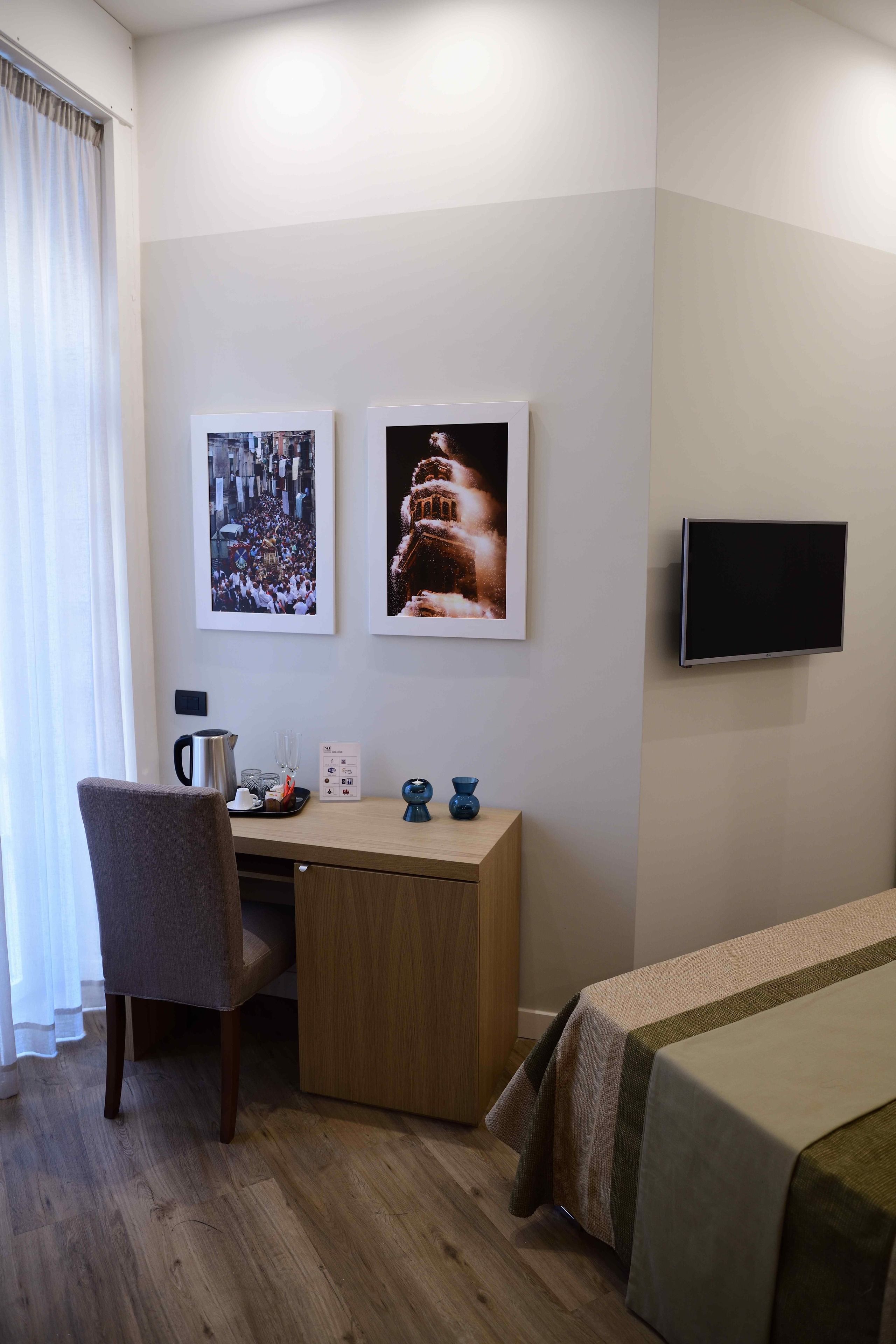 Una habitación de hotel con un escritorio de madera, una silla, una cama con cubrecama a rayas, un televisor de pantalla plana en la pared y dos cuadros enmarcados.